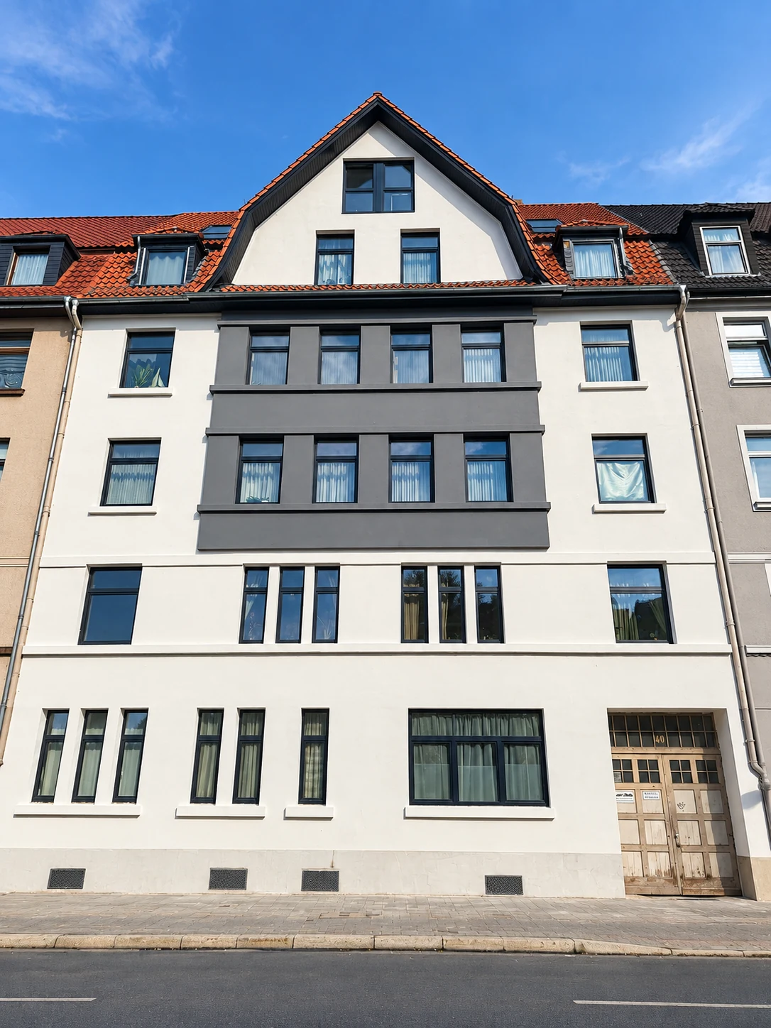 Saniertes Mehrfamilienhaus mit heller Fassade und dunklen Fensterakzenten
